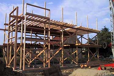 Das Rundholz-Ständergerüst wird aufgestellt, dann folgt das Dach: so können die Strohballenwände im Trockenen errichtet werden.